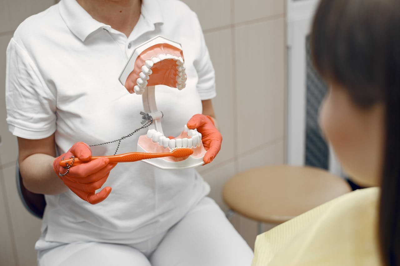 services-02 A dentist shows proper brushing technique using a dental model to a patient in a clinic.