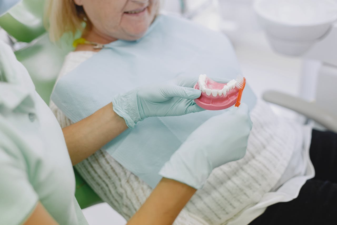 services-01 Senior woman in dental chair being shown denture brushing technique by a dental professional.